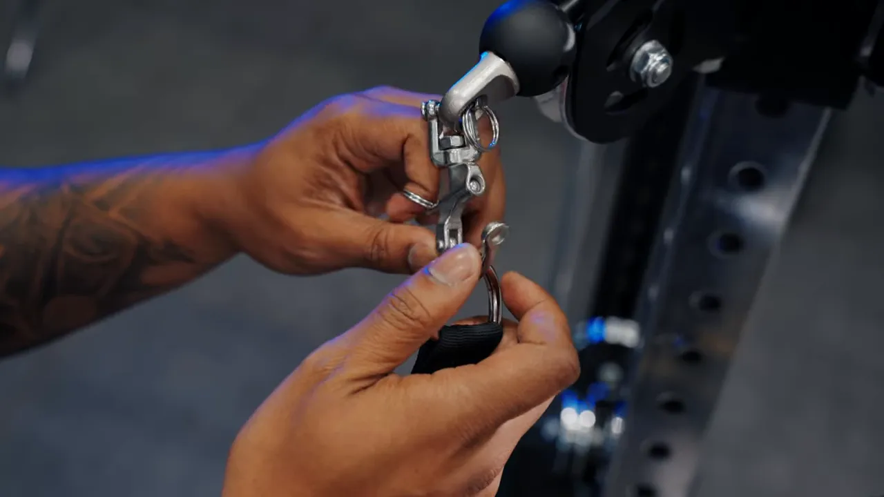 close-up of hands connecting a swivel shackle and carabiner to a cable machine pulley