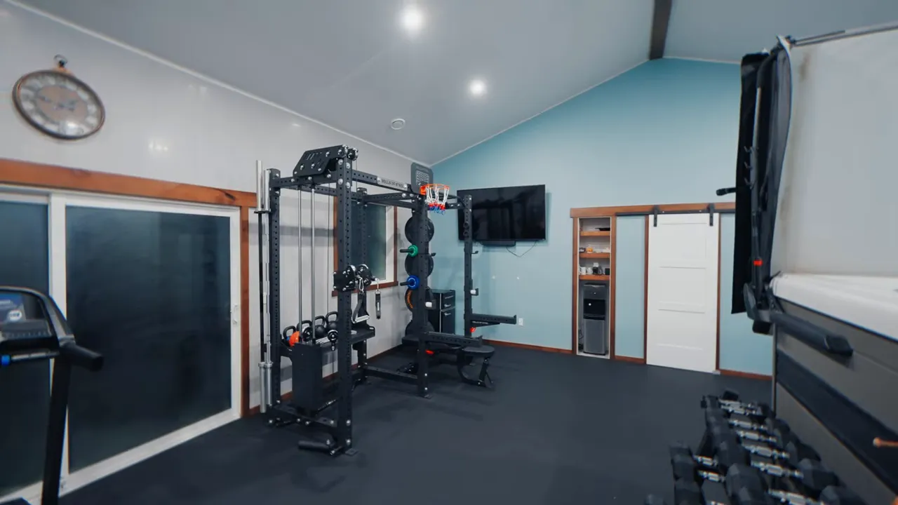 wide shot of the finished home gym showing a power rack, treadmill, TV, storage and dumbbells
