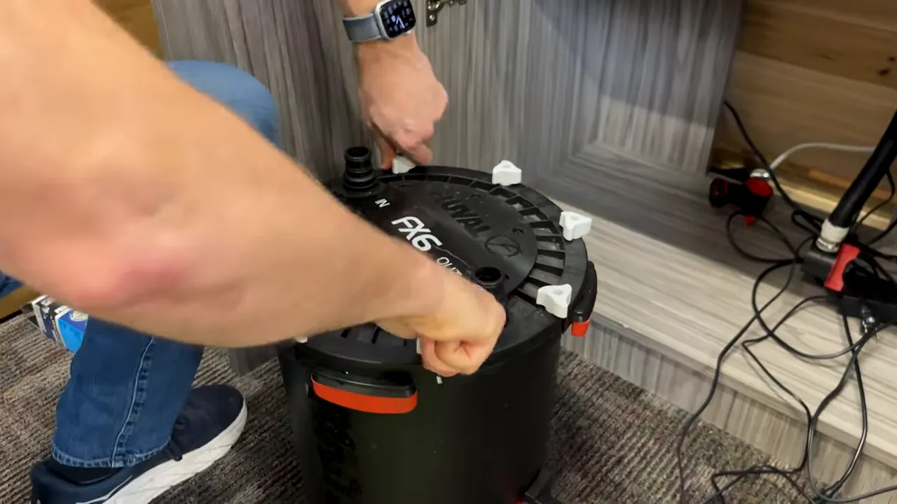 Hands fastening opposite white lid clamps on a closed Fluval FX6 canister
