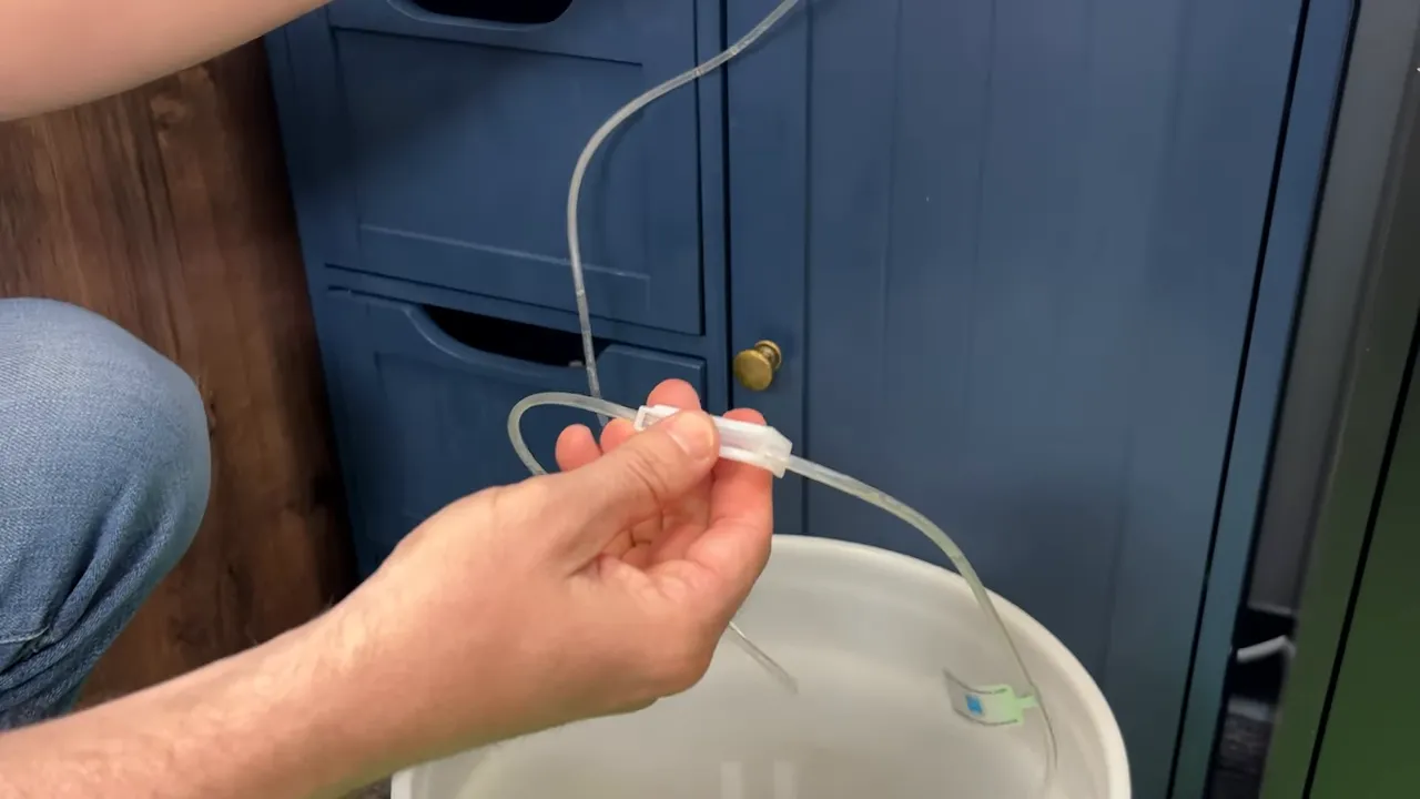 Hands adjusting a small white clamp on clear drip acclimation tubing above a bucket