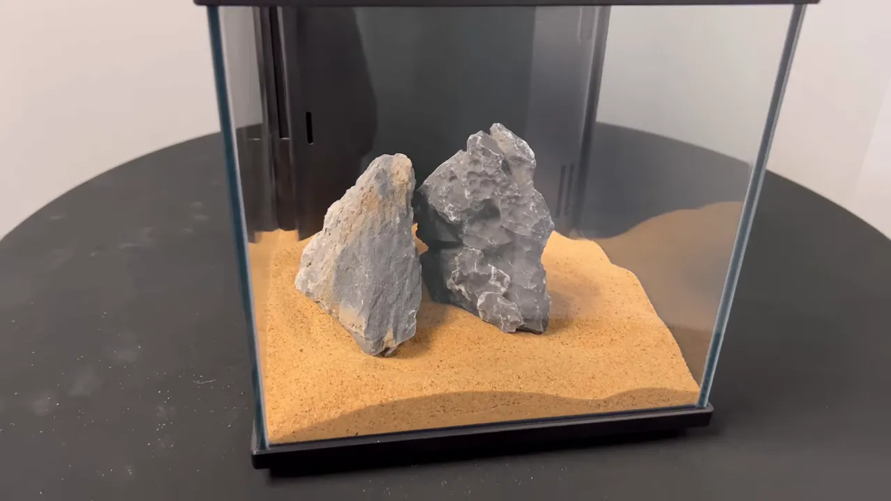 Small cube aquarium with gold sand and two grey stones arranged inside