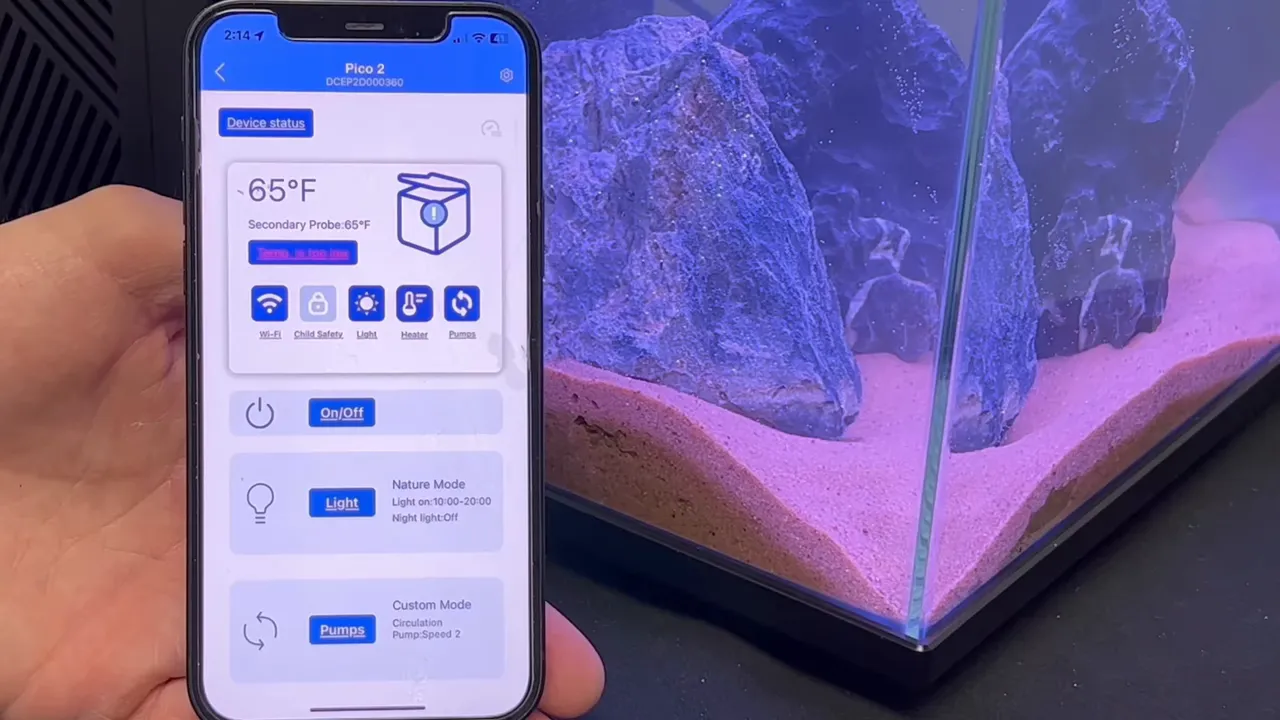 Smartphone displaying Pico Cube aquarium control dashboard beside illuminated aquarium