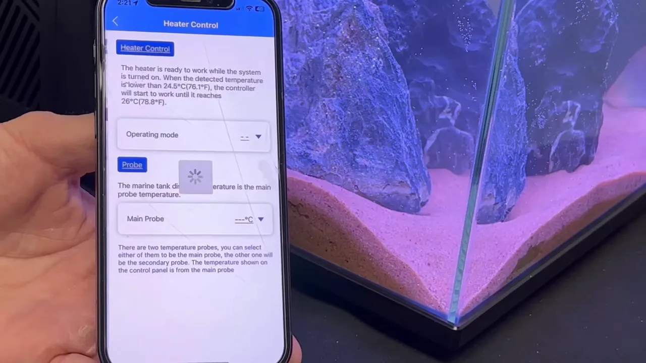 Smartphone showing heater settings beside purple illuminated aquarium