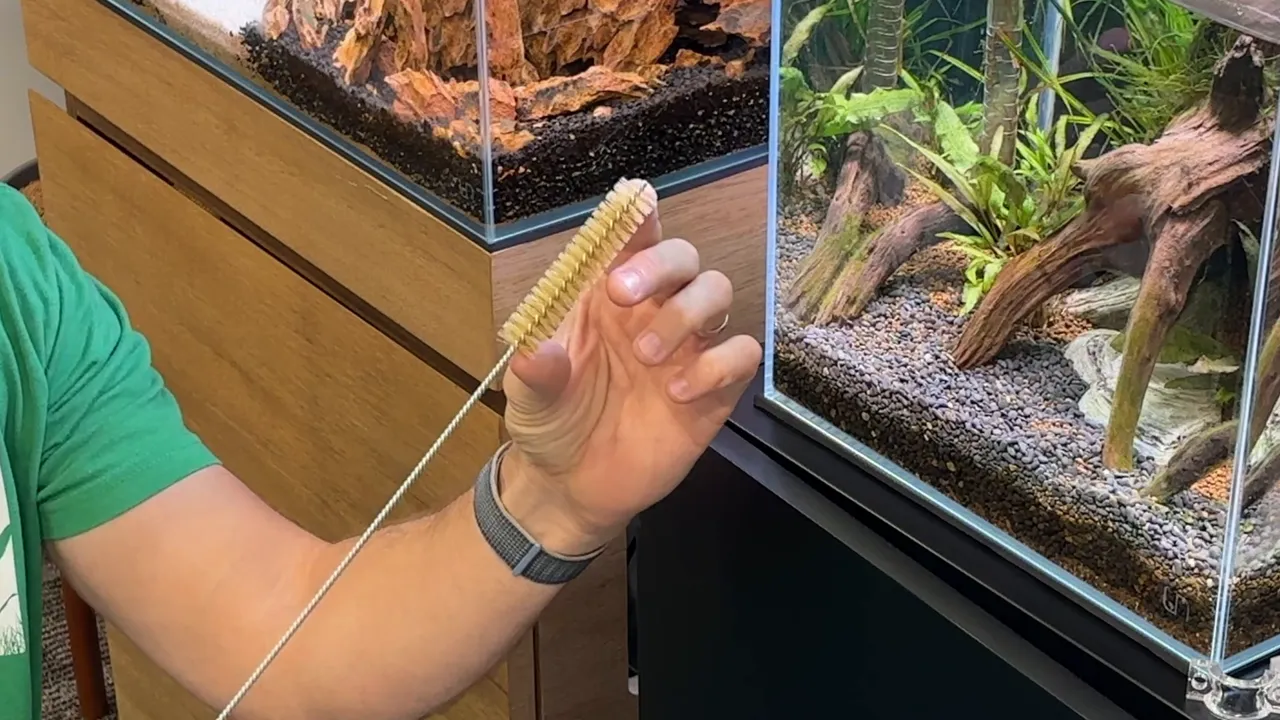 Long flexible cleaning brush with yellow bristles held beside an aquarium