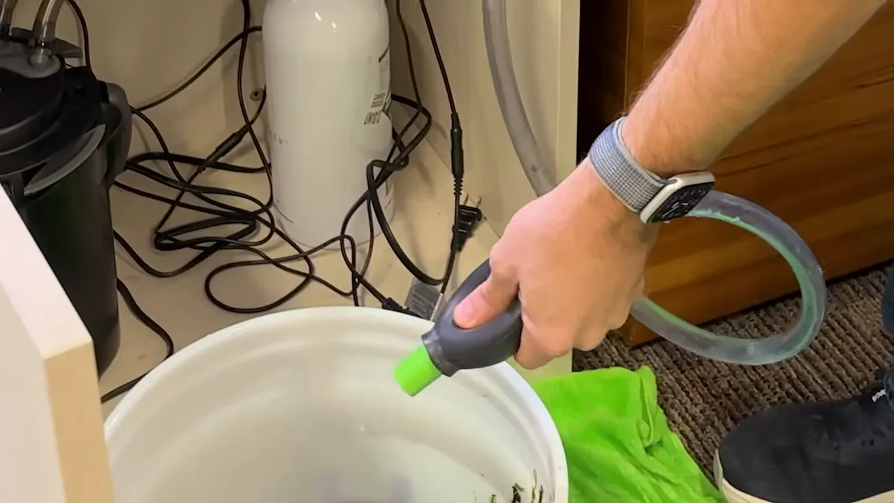 Hand holding a grey and green priming bulb over a white bucket