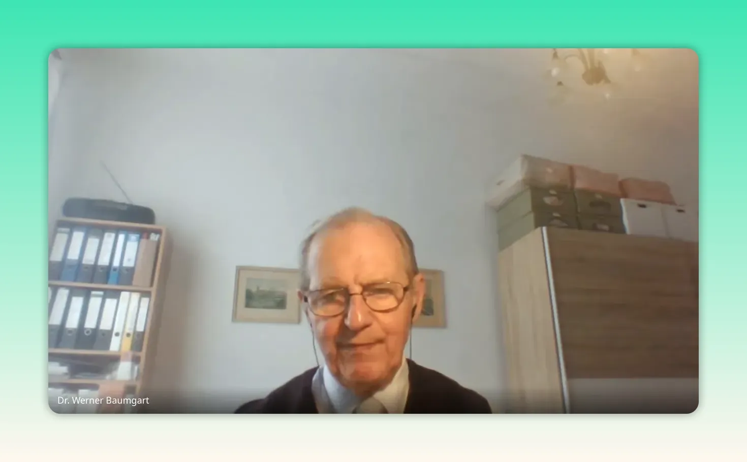 Experte spricht im Videointerview mit neutralem Gesichtsausdruck, Regal im Hintergrund