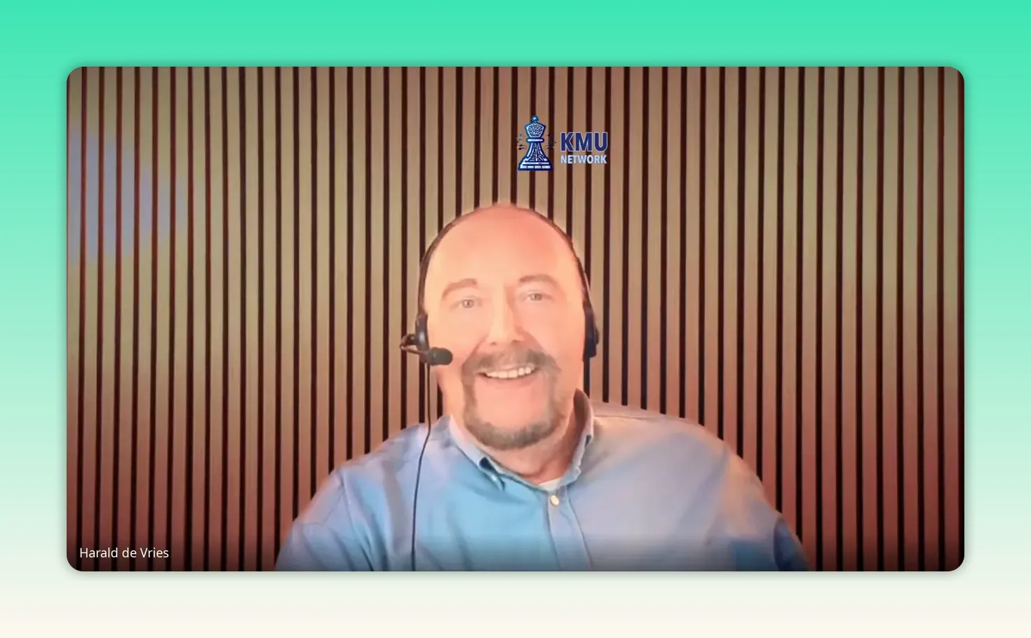 Klare Aufnahme eines Sprechers mit Headset vor gestreifter Holzpaneelwand und Logo