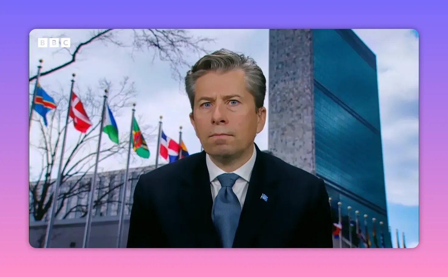 Intervenant en interview devant le bâtiment du siège des Nations Unies et une rangée de drapeaux.