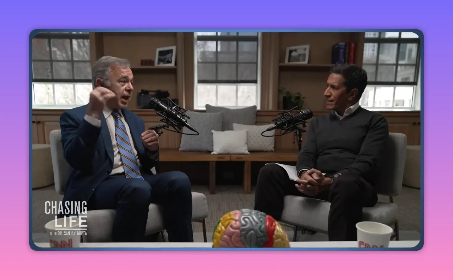 Podcast-Interview mit zwei Experten, einer gestikuliert deutlich, Gehirnmodell im Vordergrund.