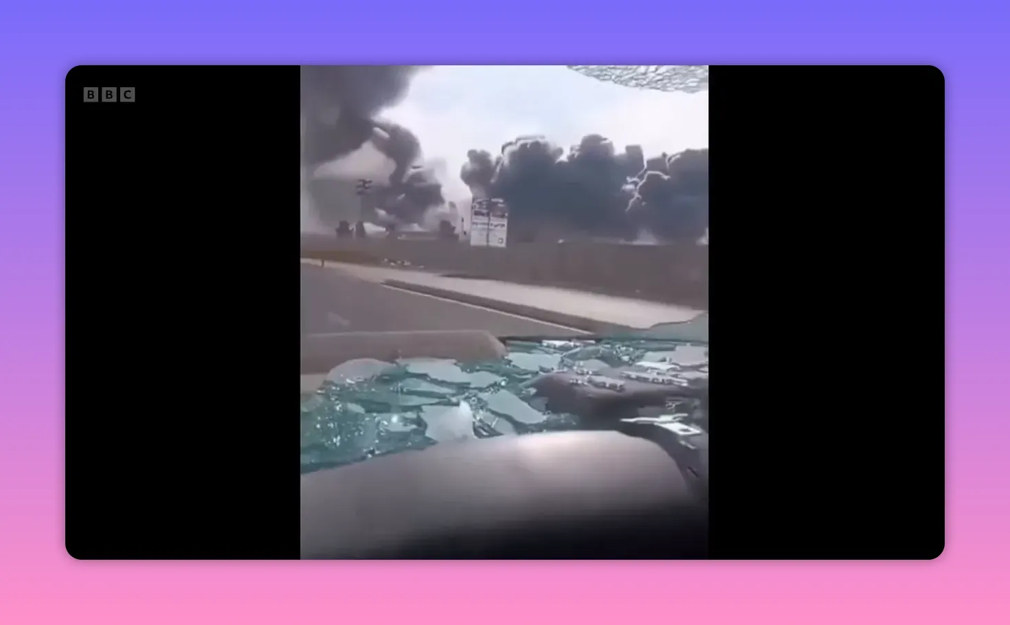 Épais nuages de fumée noire au‑dessus d’un site attaqué, vu à travers un pare‑brise brisé