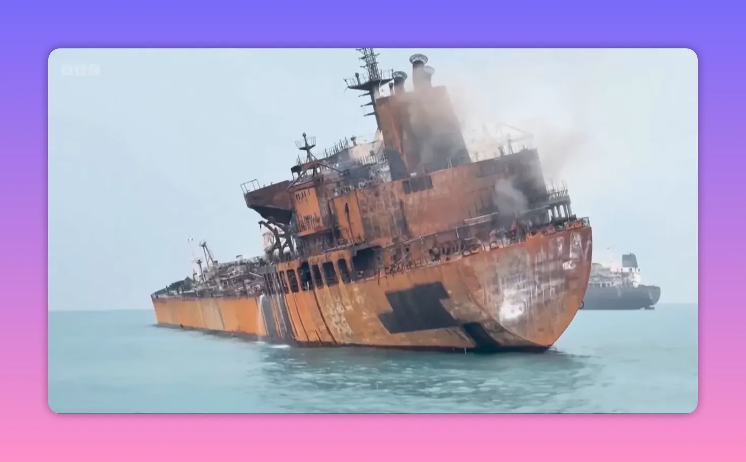 Pétrolier lourdement endommagé avec fumée s'échappant, vu de côté en pleine mer avec un autre navire en arrière-plan.