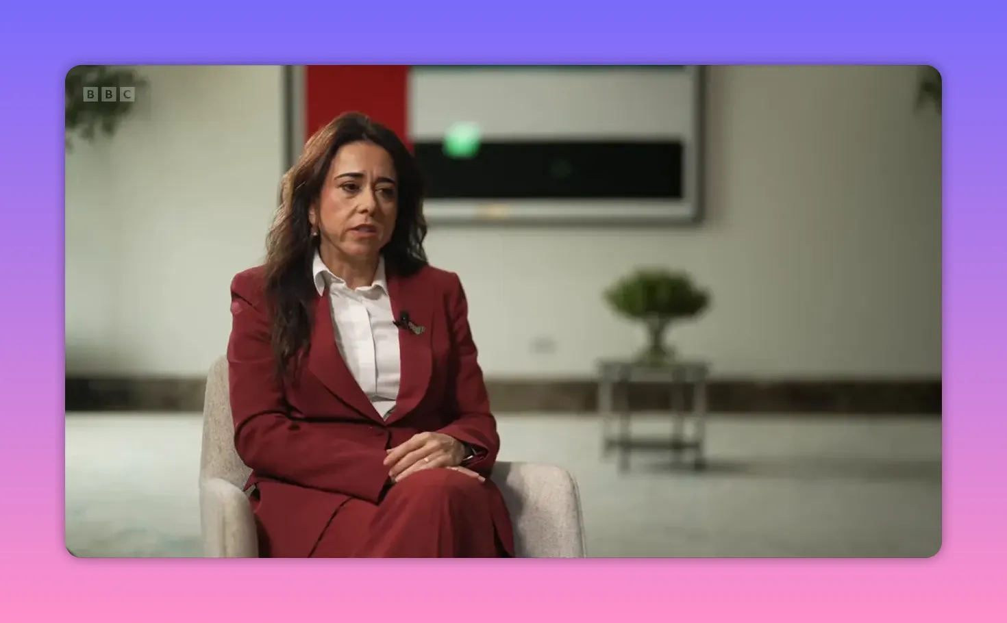 Femme en costume bordeaux assise dans un fauteuil donnant une interview dans un décor institutionnel.