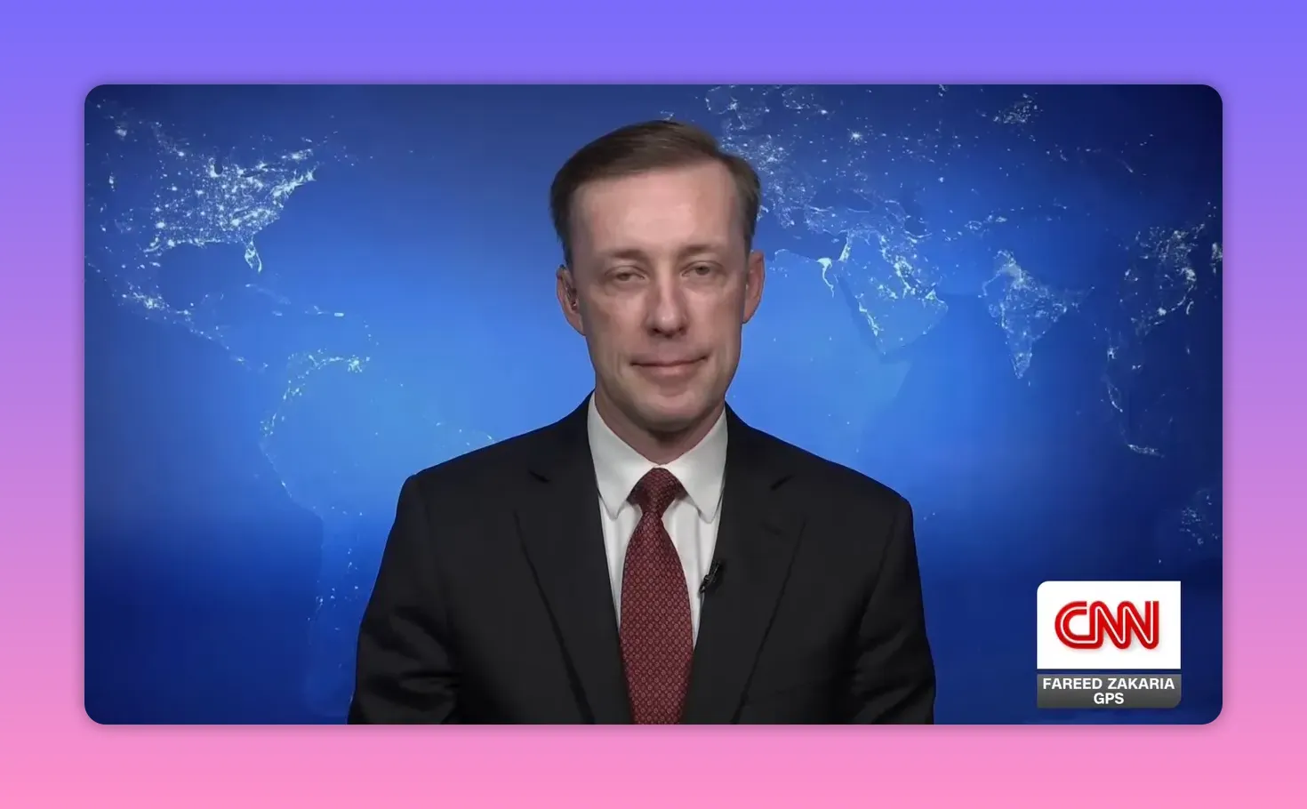 Interviewgast in Anzug vor blauem Weltkarten-Hintergrund, mittlere Aufnahme, klare, ruhige Bildkomposition.