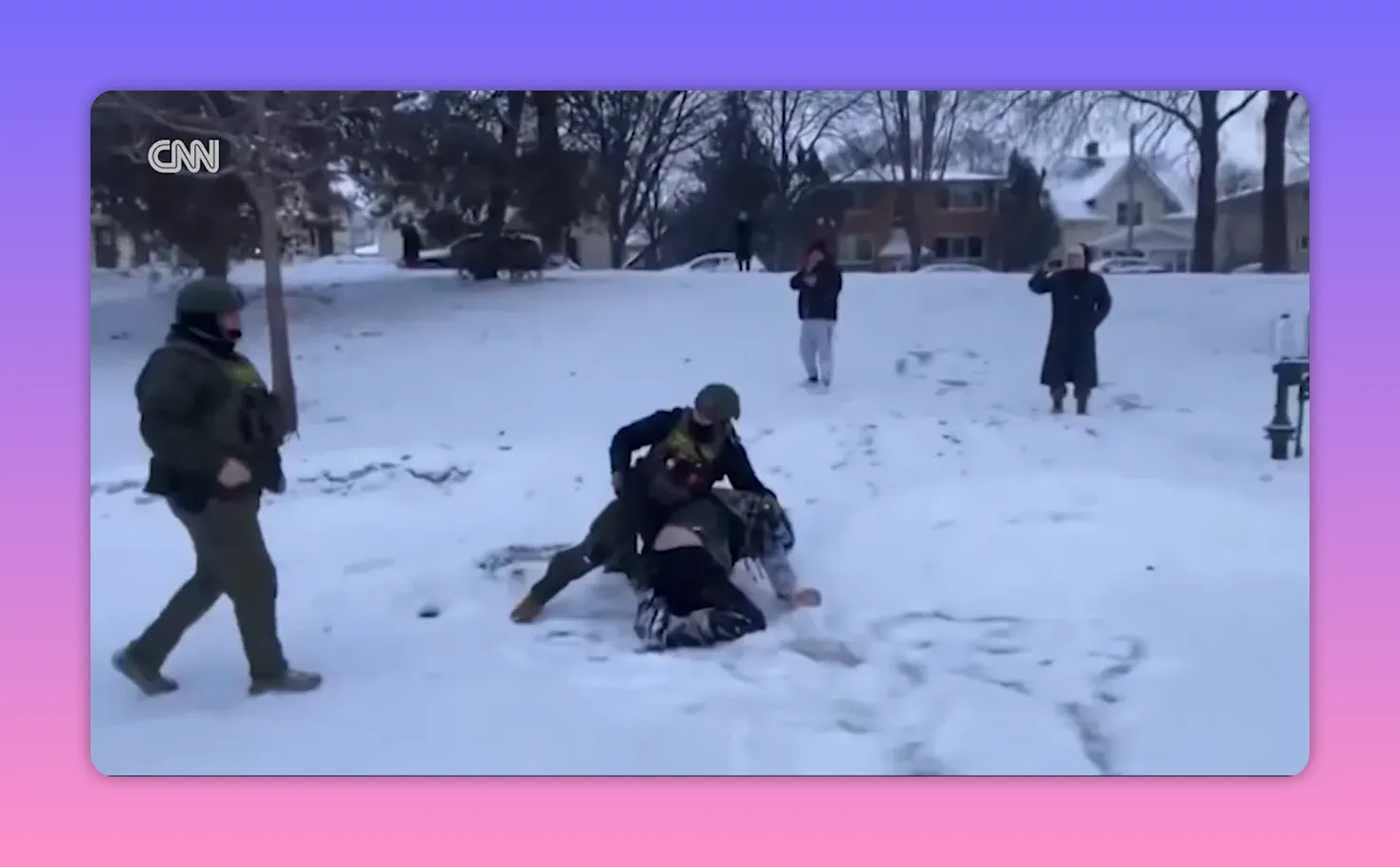 Zwei vermummte Einsatzkräfte drücken eine Person im Schnee zu Boden; mehrere Zuschauer filmen mit Smartphones.