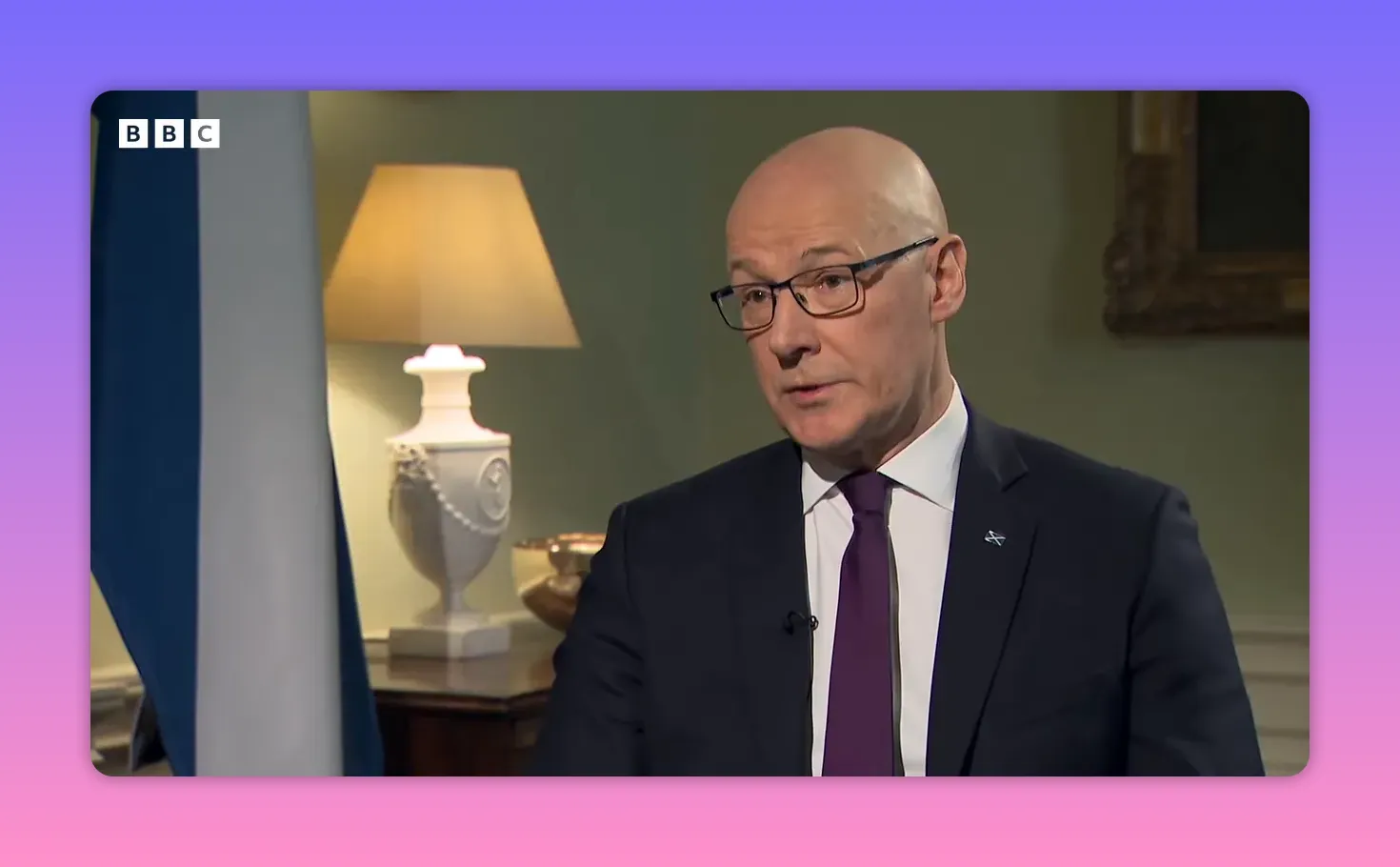 Portrait serré d'un homme en costume pendant une interview, drapeau écossais et lampe visibles