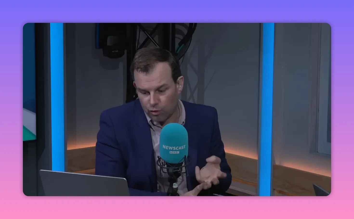 Animateur de radio en studio parlant devant un micro turquoise 'Newscast' avec ordinateur et gestes de la main visibles