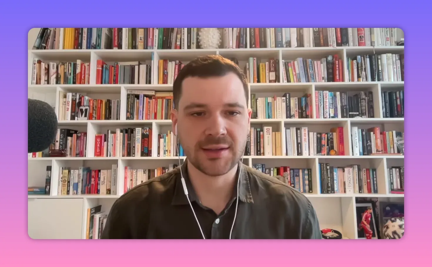 Commentateur en gros plan devant une étagère de livres, micro à gauche