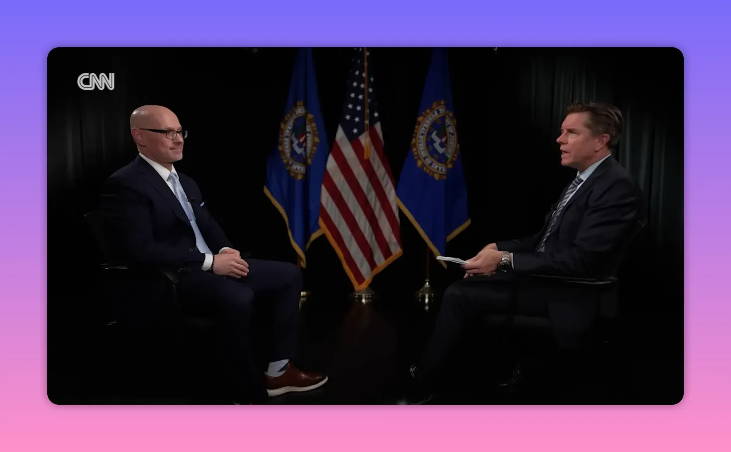 Zwei Personen im Interview vor US-Flagge und Dienstsiegeln