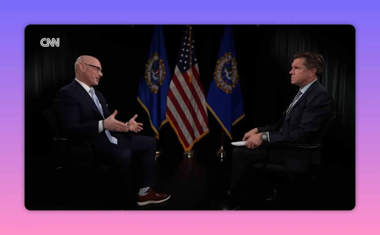 Zwei Personen im Gespräch, links gestikulierender Experte, US-Flagge im Hintergrund