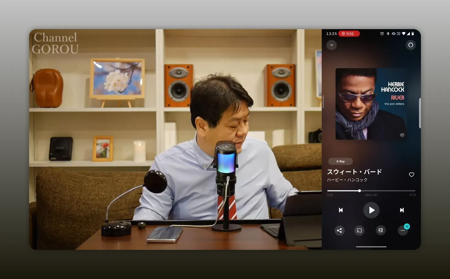 テーブル上のマイクとスマホの音楽アプリ。画面に表示されたアルバムアートが鮮明で、字幕や大きな文字が重なっていないクリアな写真。