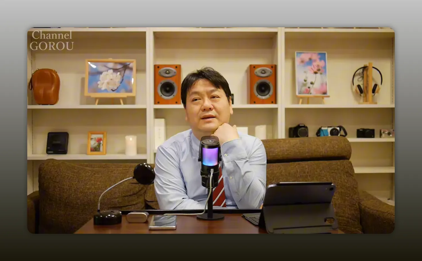 あごに手を当てて考えながら話す司会者のスタジオ写真(字幕なし、レビューの結びに使いやすい)