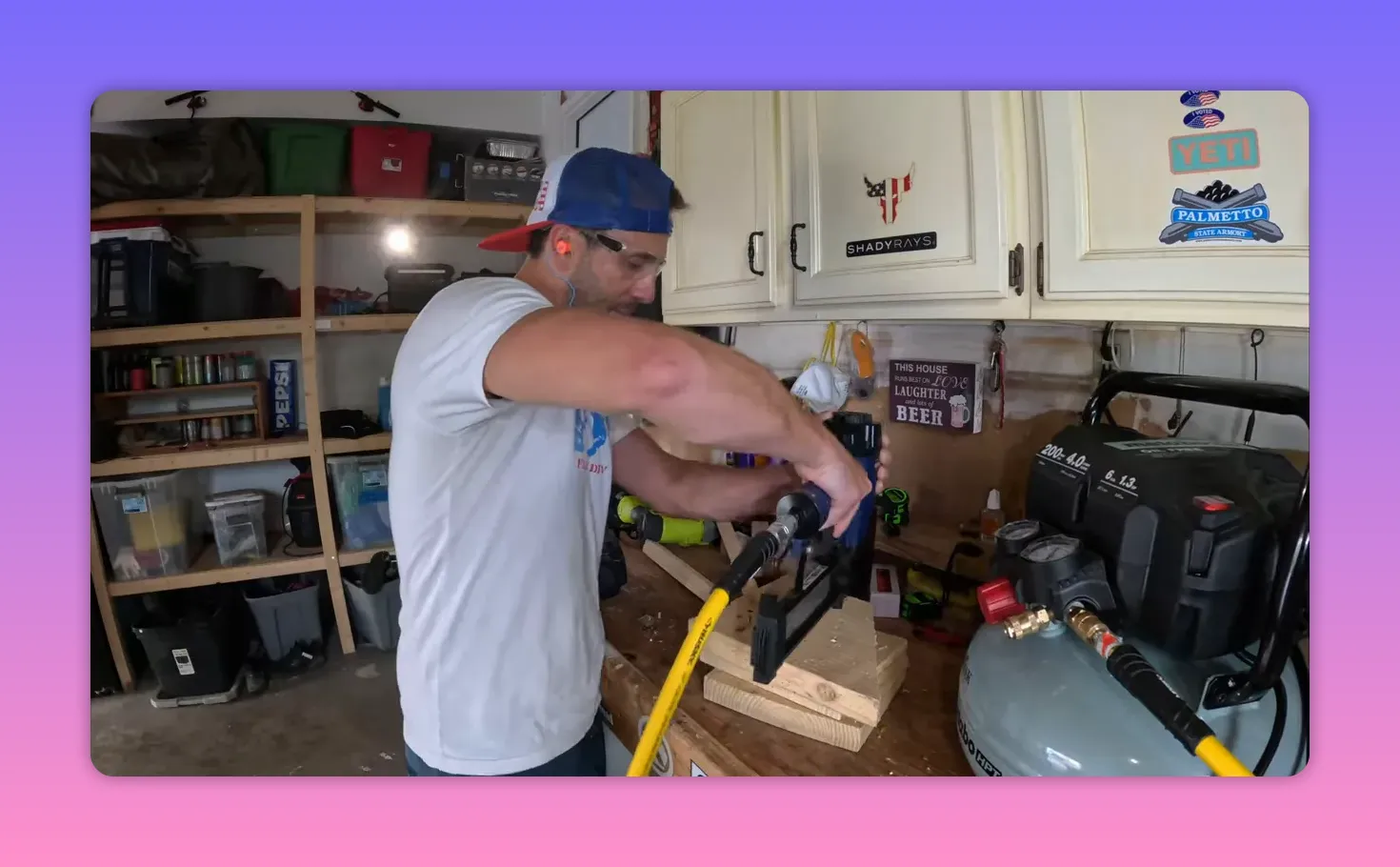 Framing nailer firing into stacked lumber with a yellow hose connected to a 6-gallon pancake air compressor showing gauges