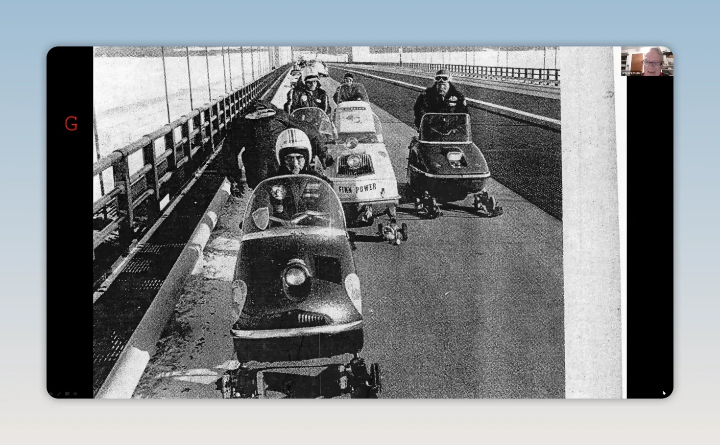 vintage black-and-white photo of multiple riders on early snowmobiles crossing a bridge