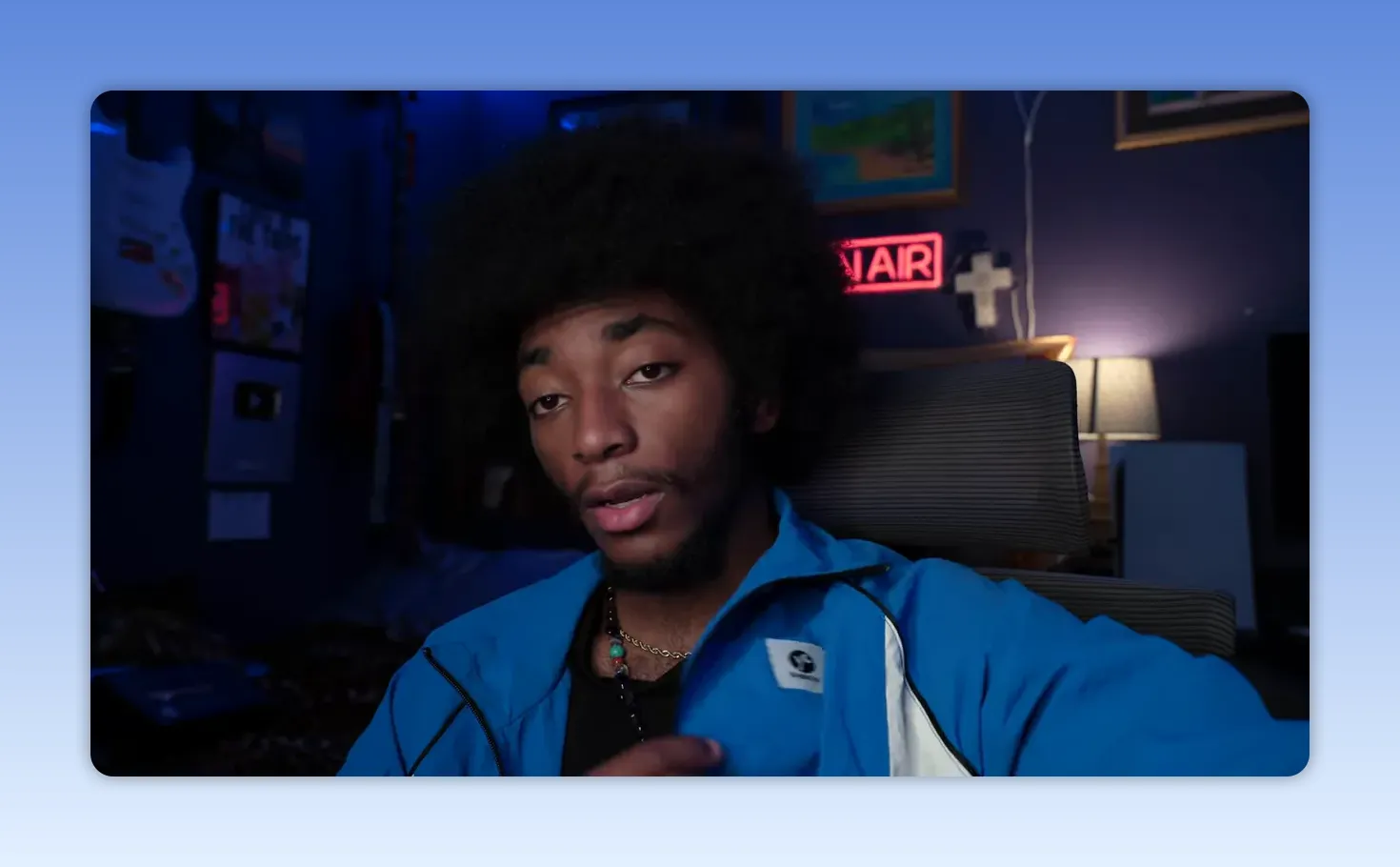 Plan moyen d'une personne en veste bleue, gestuelle légère, panneau lumineux 'ON AIR' en arrière-plan.