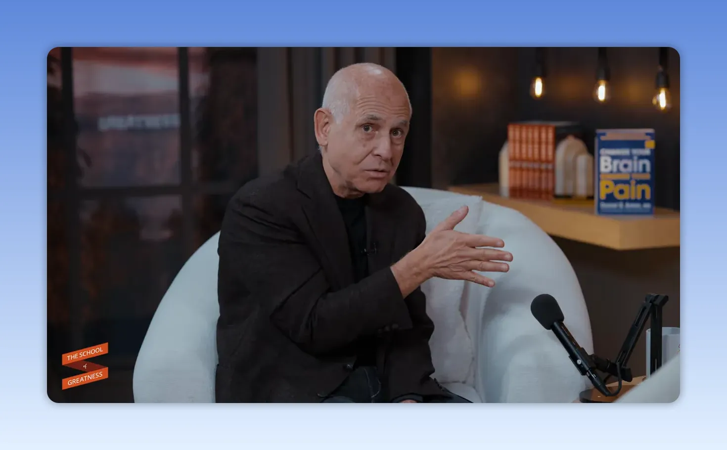 Intervenant parlant et faisant un geste explicatif de la main, image nette avec livre sur le cerveau en arrière-plan