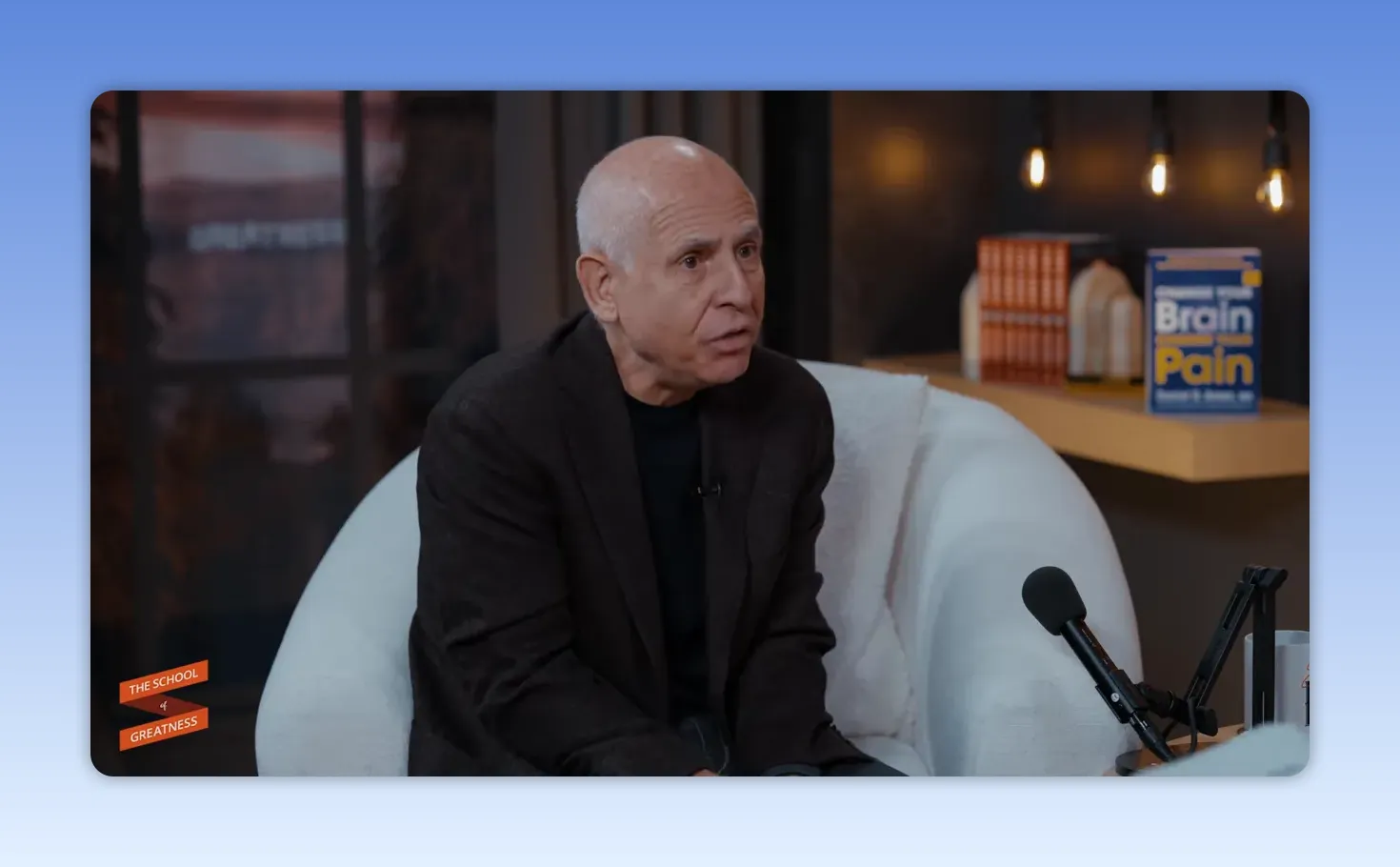 Plan large d'un intervenant en studio, micro sur la droite et le livre 'Brain Pain' visible en arrière‑plan