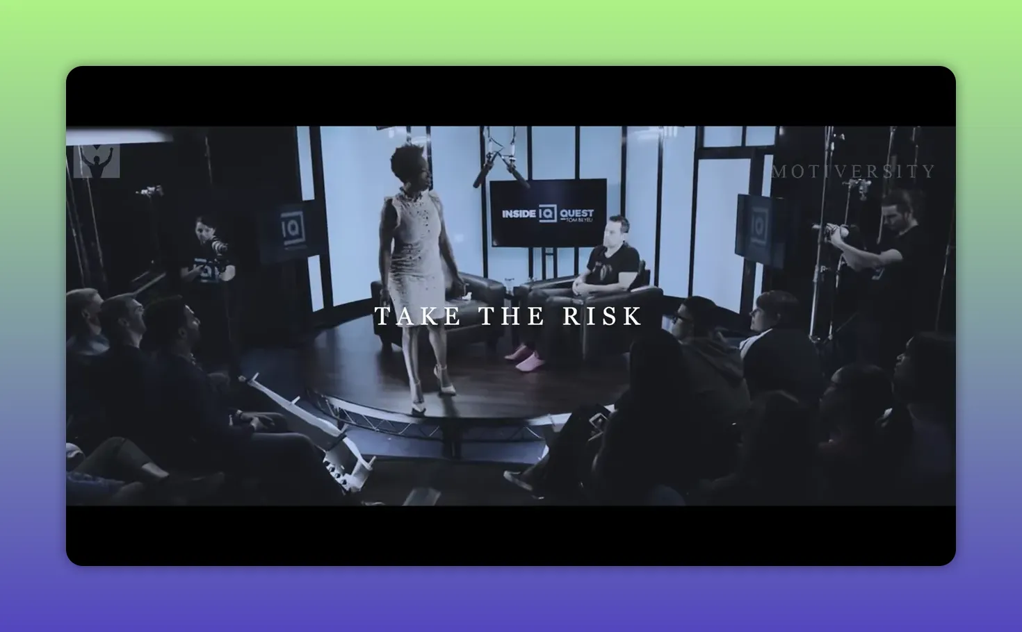 Speaker sul palco in studio che parla davanti al pubblico con il testo 'TAKE THE RISK' in sovrimpressione.