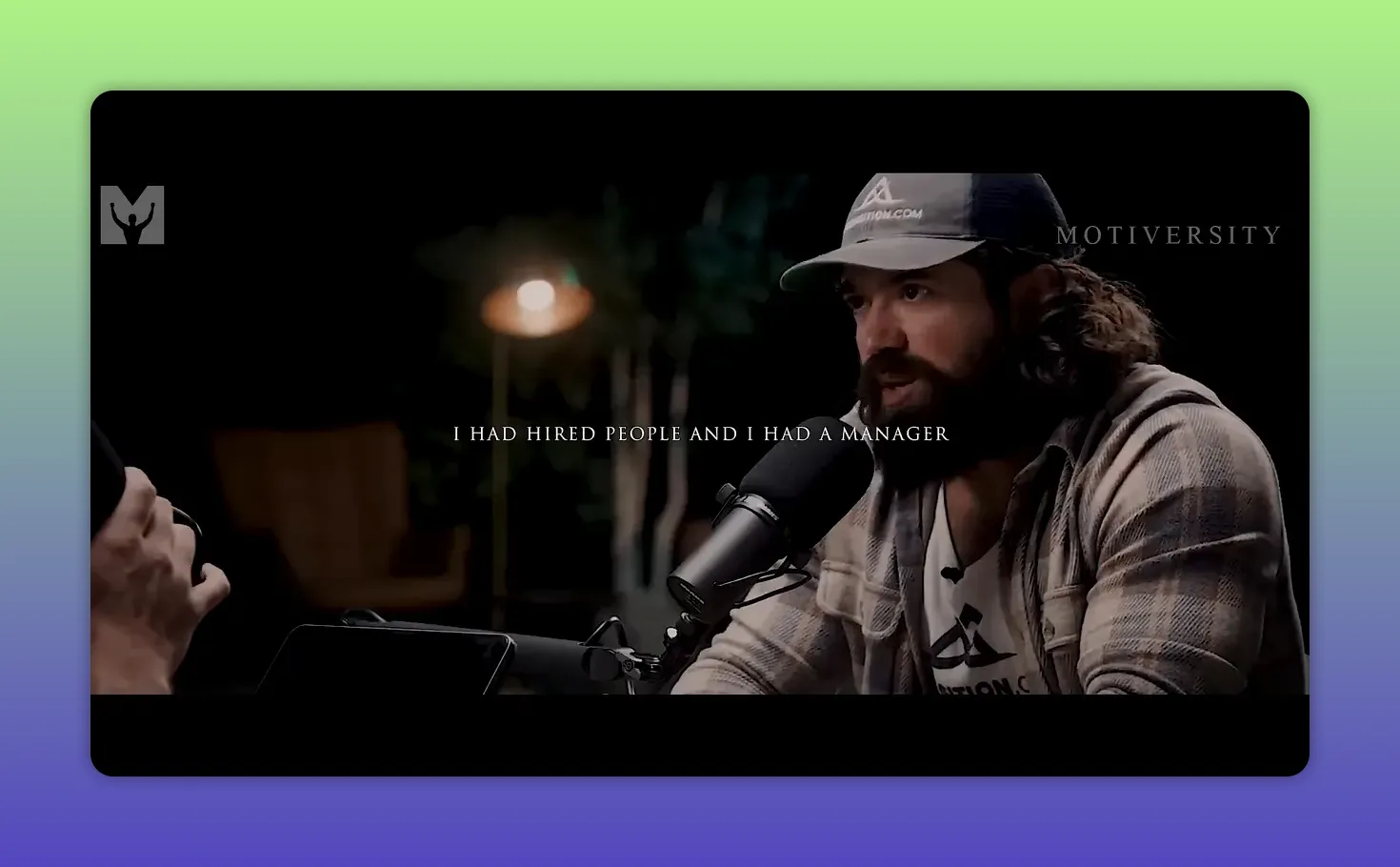 Intervistato al tavolo con microfono, ambiente dello studio e luce calda sullo sfondo