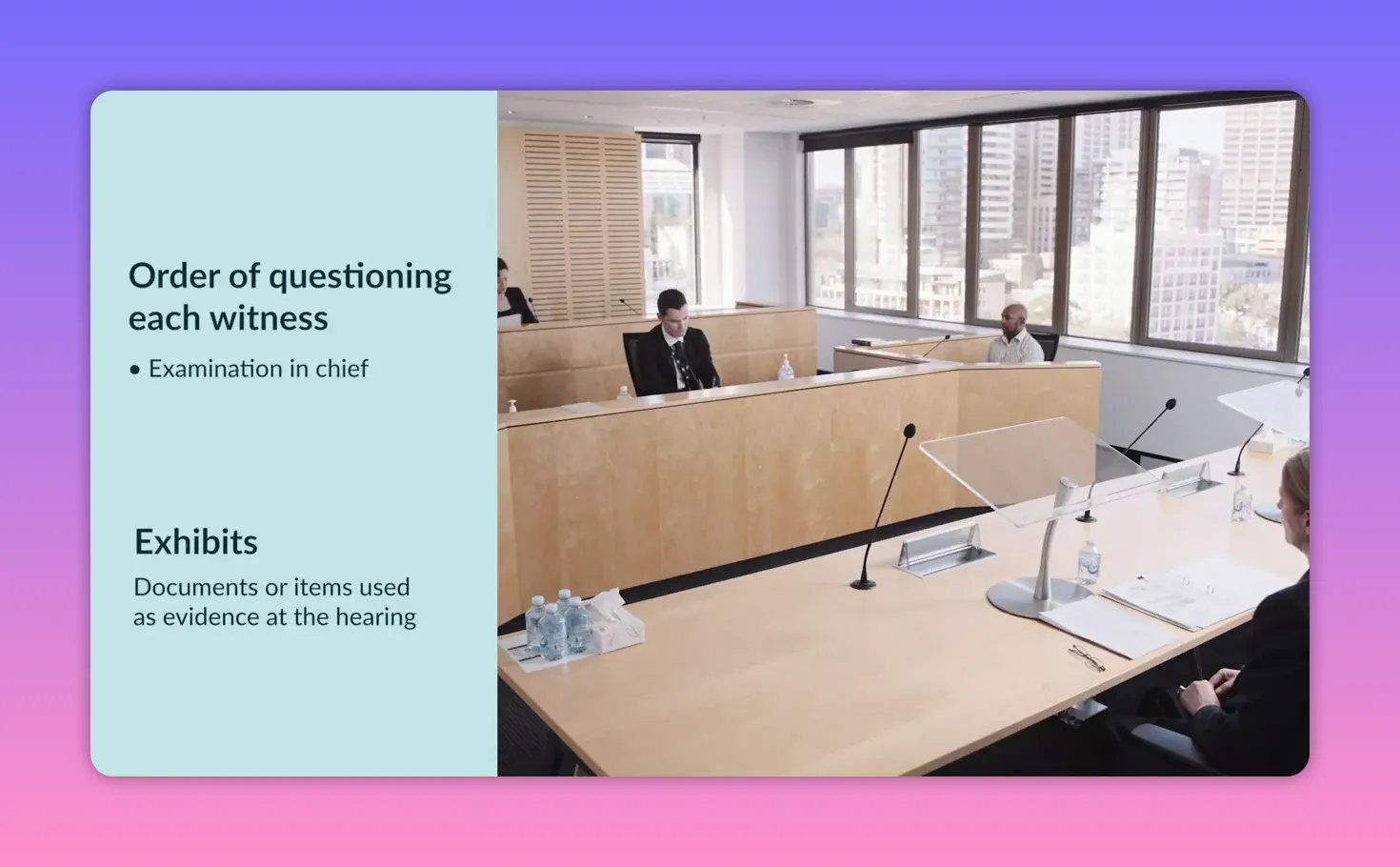 Wide shot of a hearing room with bar table, lecterns, microphones and documents and water bottles on the table; city windows in the background.