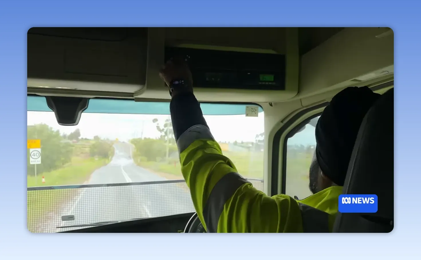 Truck driver reaching up toward the overhead console, appearing to adjust a radio or device while driving.