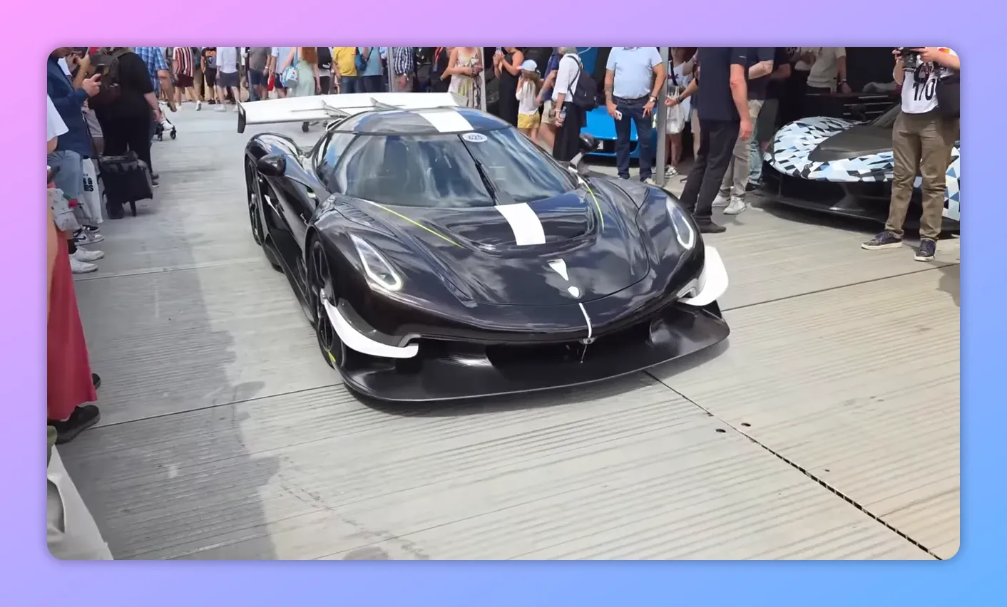 Vista frontale nitida di una Koenigsegg esposta al Supercar Paddock con pubblico e stand sullo sfondo.