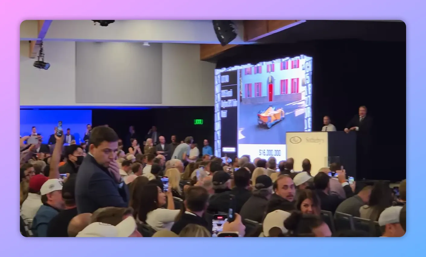 Pubblico all'asta con sullo schermo la proiezione di una supercar arancione che percorre una strada