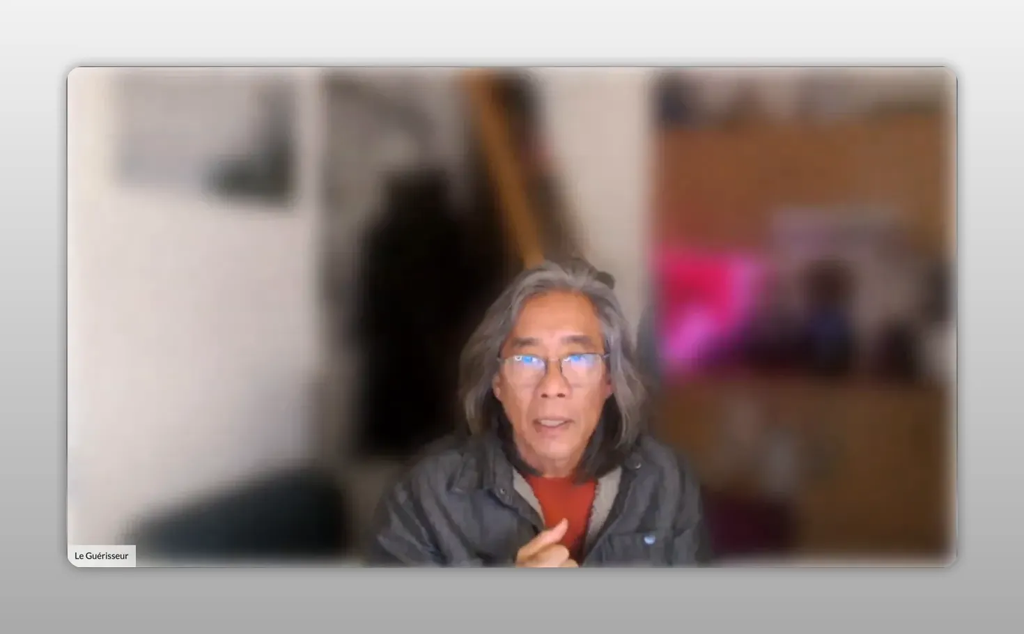 Intervenant en webcam, visage net et main légèrement en mouvement, fond flou