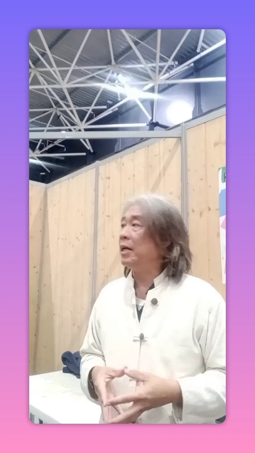 Intervenant formant un petit triangle avec les mains, posture ouverte devant des panneaux en bois.