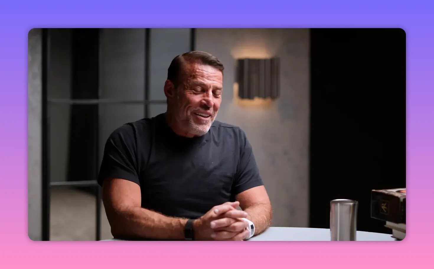 Host seated at a table with eyes closed and hands clasped, a calm reflective portrait in warm studio lighting.