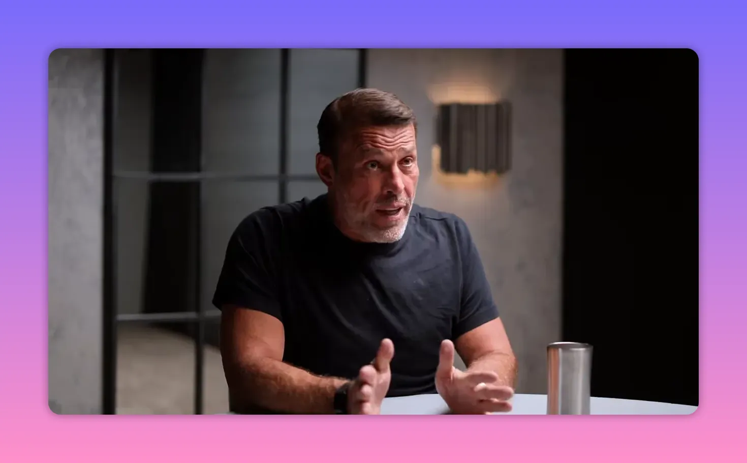 Host using both hands in a explaining gesture while seated at a table, well-lit studio portrait.