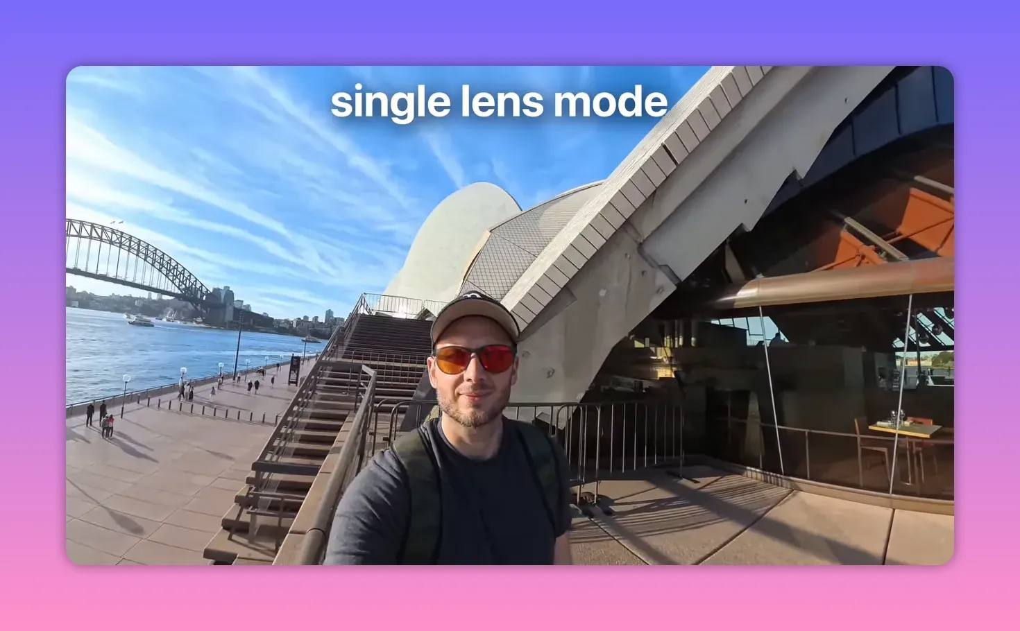 Selfie POV shot in single‑lens mode showing a presenter with sunglasses, the Sydney Opera House and Harbour Bridge in the background