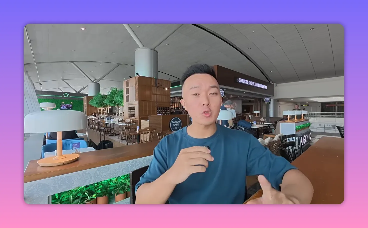 Host speaking in an airport cafe with lamps, seating and a Saigon Cafe sign clearly visible