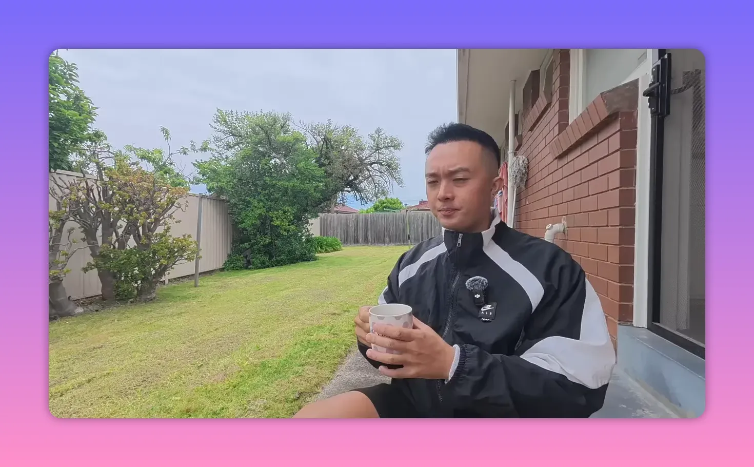 Person seated on a porch holding a coffee mug with both hands, backyard visible