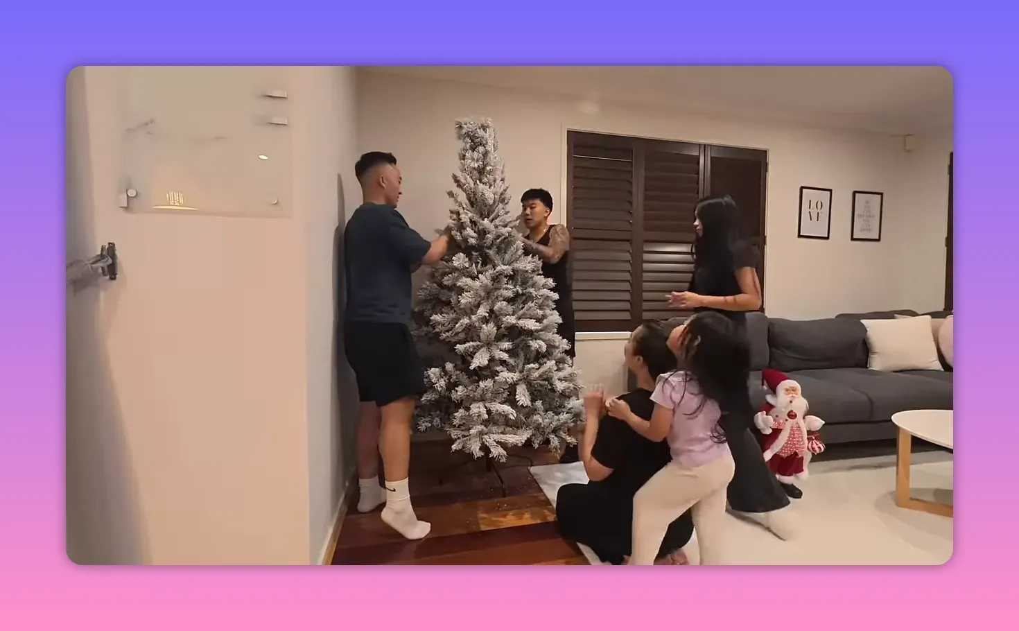 Group of family members arranging and fluffing a frosted Christmas tree together in the living room
