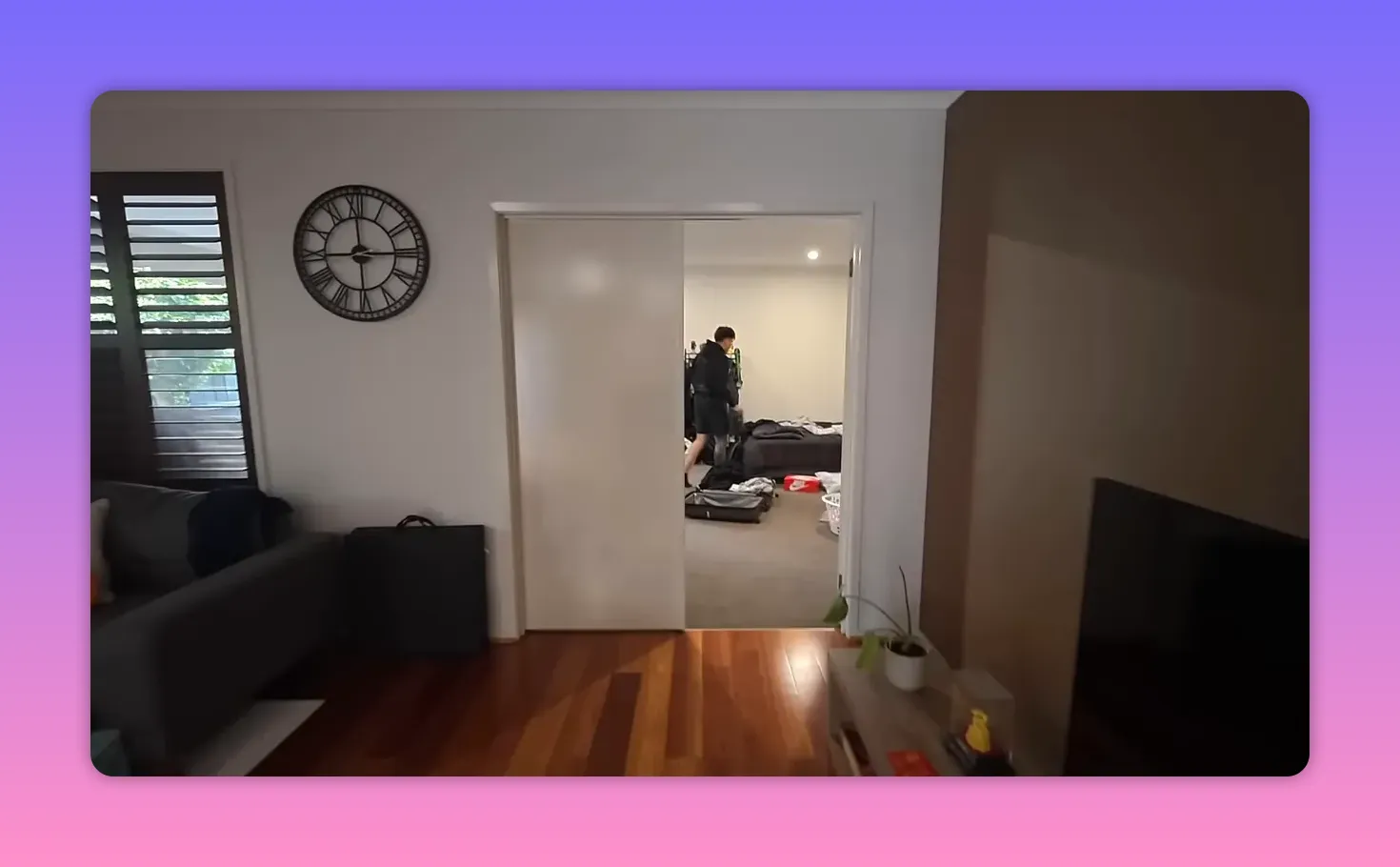 Open doorway into a bedroom with suitcases on the floor and a person packing, viewed from the living area