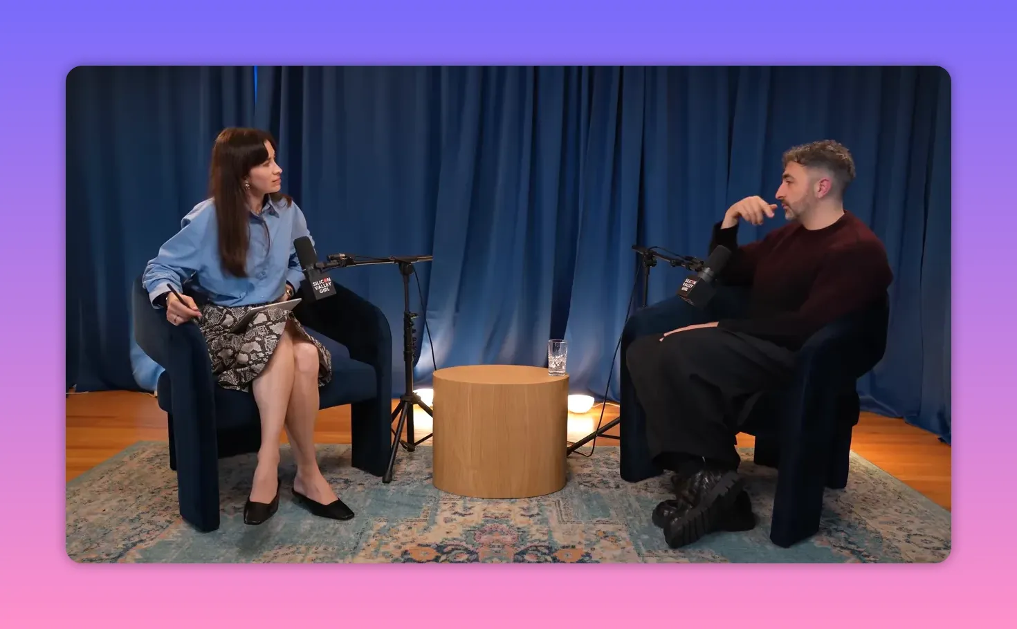 Podcast host taking notes while listening to guest on a small studio set with blue curtains