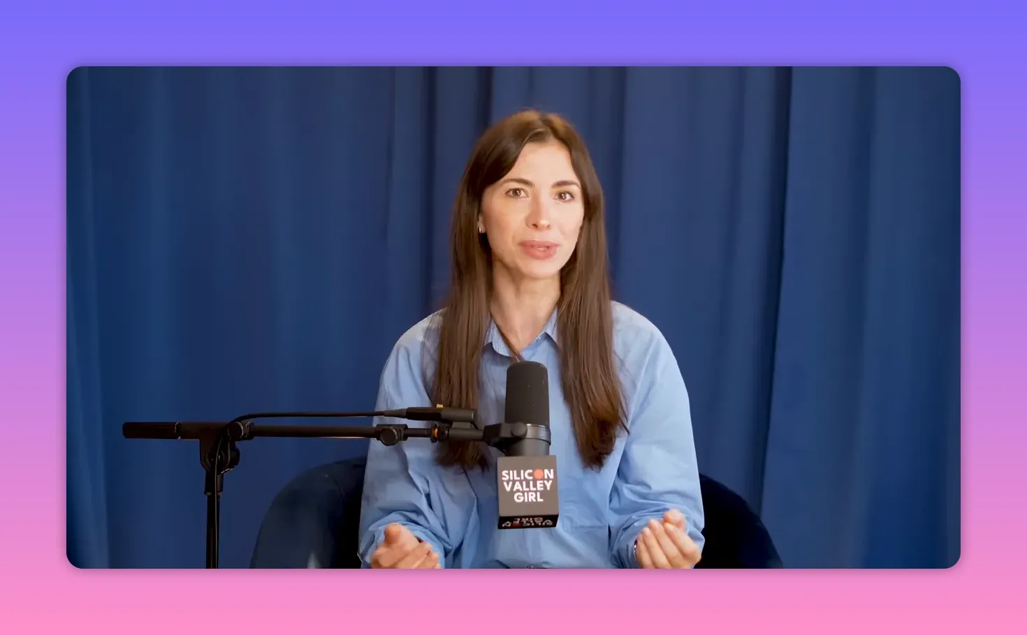Podcast host seated with a microphone in front of a blue curtain, speaking during an interview.