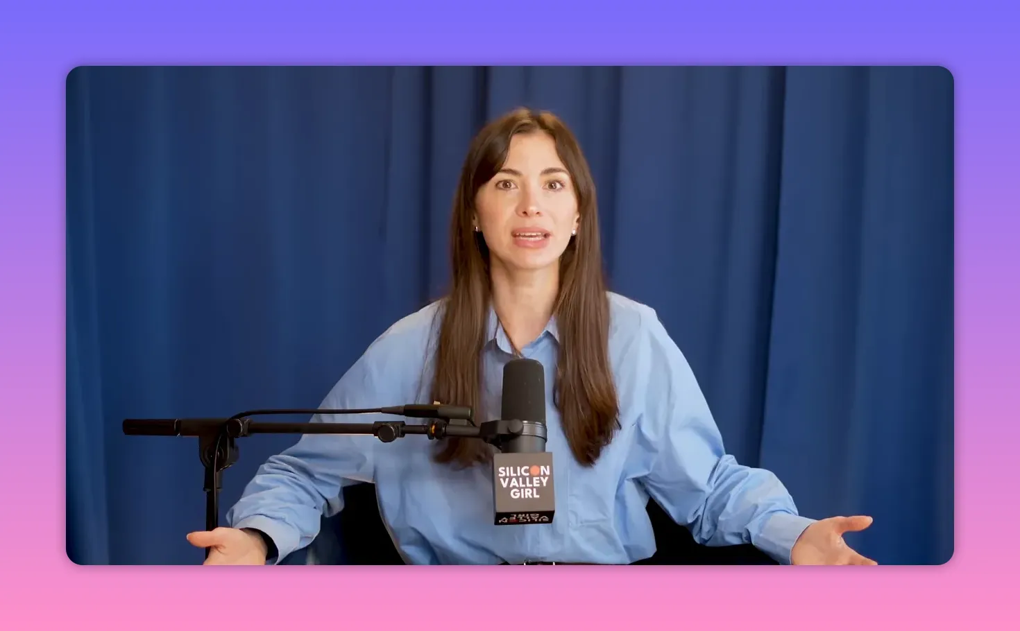 Medium shot of a podcast host speaking and gesturing with a microphone tag visible against a blue curtain.