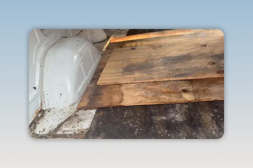 Worn plywood flooring inside the cargo van with exposed gaps and dark floor material