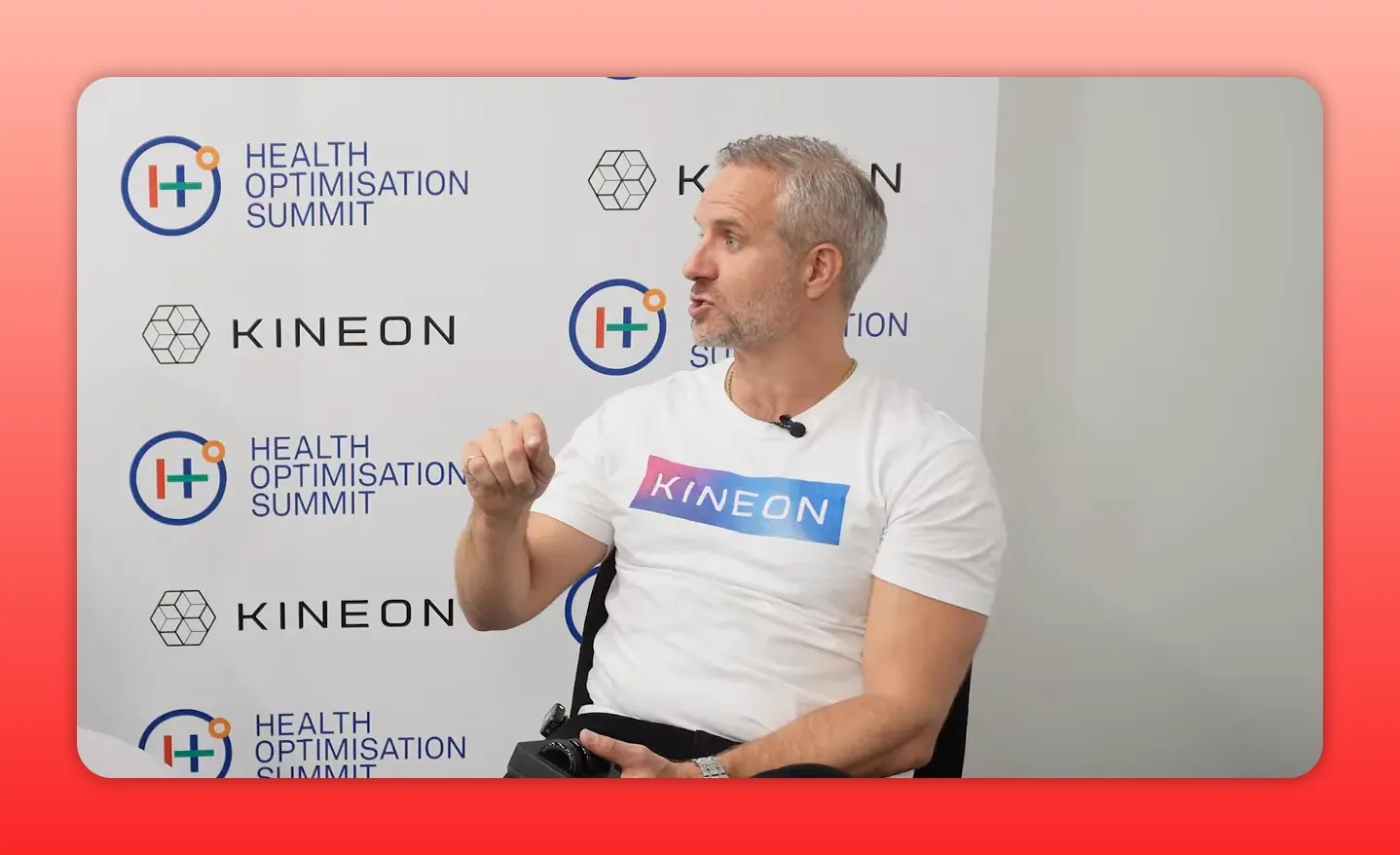 Person wearing a Kineon t-shirt gesturing and holding a modular therapy device in his lap against a Kineon backdrop.